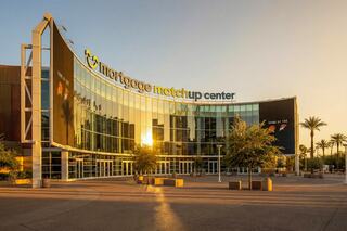 A modern building features glass façades reflecting sunlight, with palm trees nearby and a large sign reading "mortgage matchup center."