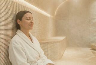 A woman in a white robe relaxes in a steamy, tranquil spa environment, embodying calm and serenity.