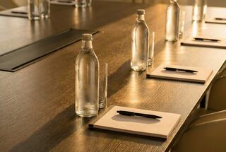 A well-prepared conference table with glass water bottles, glasses, notepads, and pens, illuminated by soft natural light.