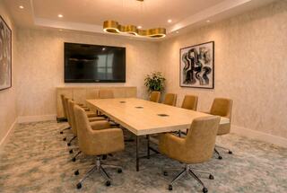 A modern conference room featuring a large table, ergonomic chairs, a wall-mounted TV, and stylish artwork, creating a professional atmosphere.