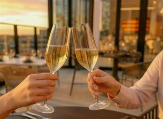 Two elegantly dressed people toast with sparkling glasses at sunset, enjoying a warm, celebratory atmosphere in a stylish setting.