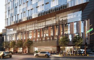 A modern glass and wood building features large windows, greenery, and bustling pedestrian activity outside, showcasing an urban environment.