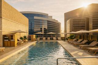 A serene rooftop pool surrounded by modern architecture, lounge chairs, and sun umbrellas, basking in warm sunset light.