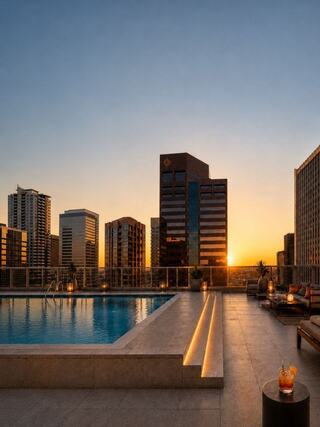 A rooftop pool overlooks a city skyline at sunset, casting warm hues across modern buildings and inviting relaxation with cozy seating.