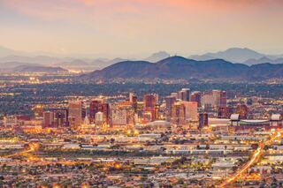 A vibrant city skyline at dusk, surrounded by mountains, with lights twinkling across the urban landscape and a colorful sky above.
