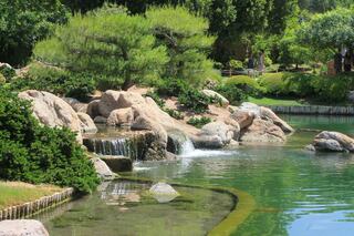A serene park scene features a gentle waterfall cascading over rocks into a tranquil green pond, surrounded by lush greenery.