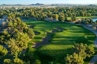 A lush green golf course stretches across the landscape, bordered by homes and mountains under a clear blue sky. Trees dot the fairway.